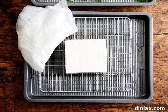 Golden Tofu and Broccoli with Savory Peanut Sesame Pesto 2 Pressing a block of firm tofu between paper towels with a heavy frying pan to remove excess water, essential for achieving crispy tofu.