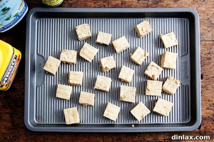Golden Tofu and Broccoli with Savory Peanut Sesame Pesto 5 Cubed tofu pieces are neatly arranged in a single layer on a parchment-lined baking sheet, prepared for roasting.
