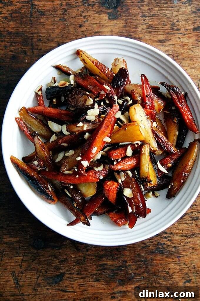 A vibrant bowl of twice-roasted carrots, glazed with honey and butter, sprinkled with black pepper and toasted almonds. The carrots are slightly charred at the edges, showcasing their caramelized sweetness and savory depth.