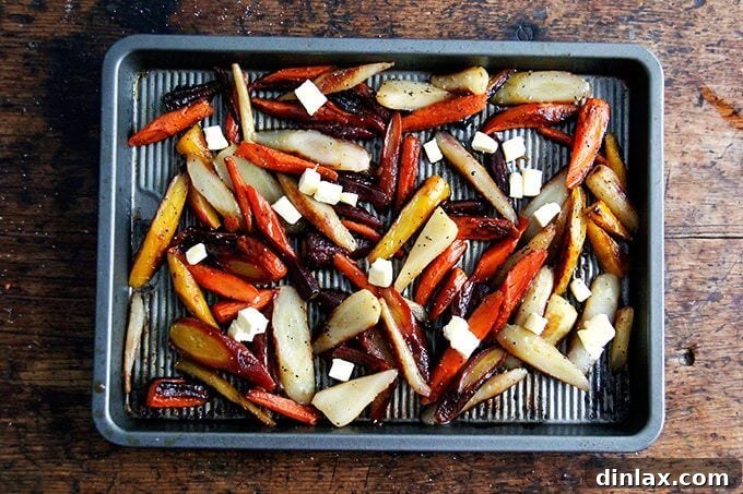 Sliced carrots spread on a sheet pan, dotted with small pieces of butter and drizzled with honey or maple syrup, prepared for their second roast.