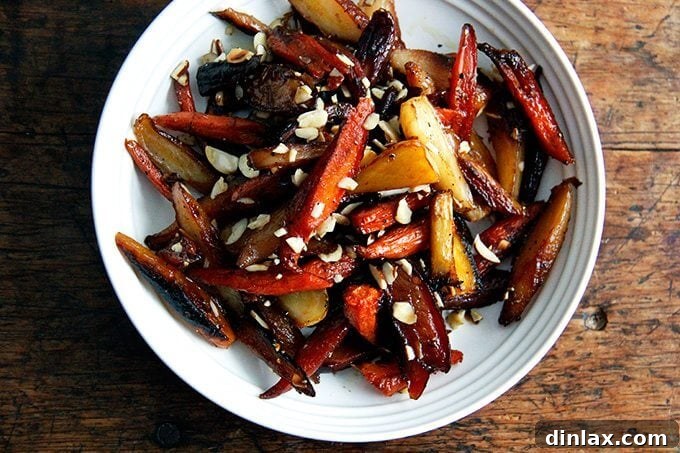 A beautiful bowl of finished twice-roasted carrots, garnished with toasted almonds, a sprinkle of salt, and freshly ground black pepper, ready to be served.