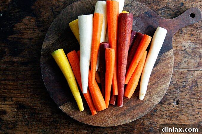 A neatly arranged pile of peeled, whole carrots on a wooden cutting board, ready for the next step in the roasting process.