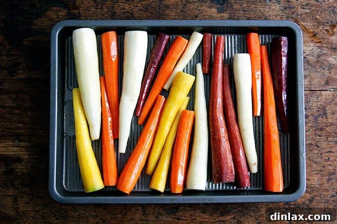 Peeled carrots glistening with olive oil, spread out on a cutting board, prepared for their first roast in the oven.
