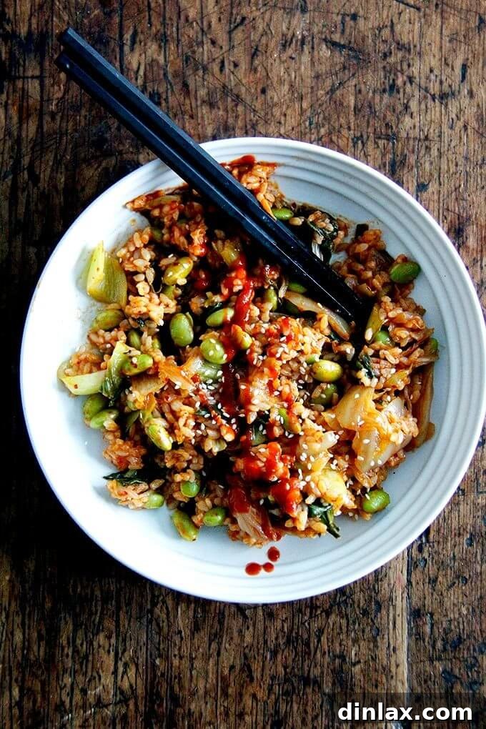 A close-up of a bowl of vegan kimchi fried rice, artistically drizzled with fiery Sriracha, adding a tempting swirl of heat.
