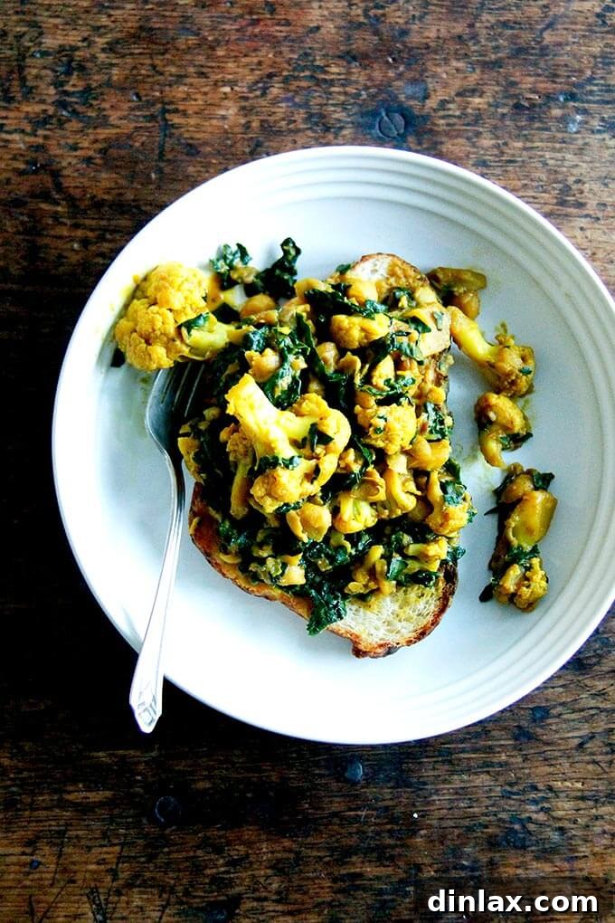 A hearty bowl featuring a vibrant chickpea and cauliflower scramble, generously mixed with fresh kale, served alongside toasted bread, showcasing a delicious and nutritious plant-based meal.
