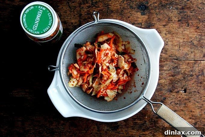 A colander filled with kimchi, allowing excess liquid to drain into a bowl below, showing the preparation for fried rice.