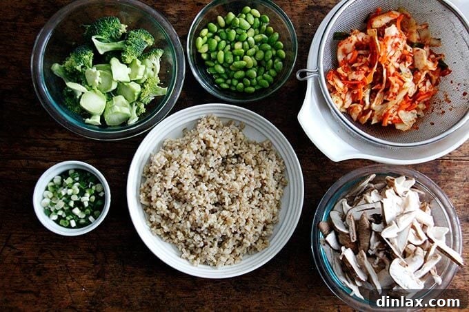 Various ingredients for kimchi fried rice are neatly prepped in separate bowls on a wooden table, including brown rice, chopped broccoli, and sliced shiitake mushrooms, ready for cooking.