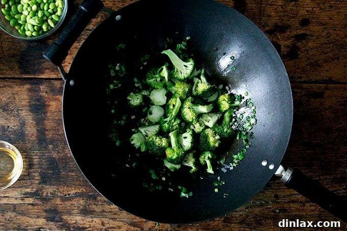 Bright green broccoli florets are stir-frying in a hot wok, showing the initial stage of vegetable cooking for the fried rice.