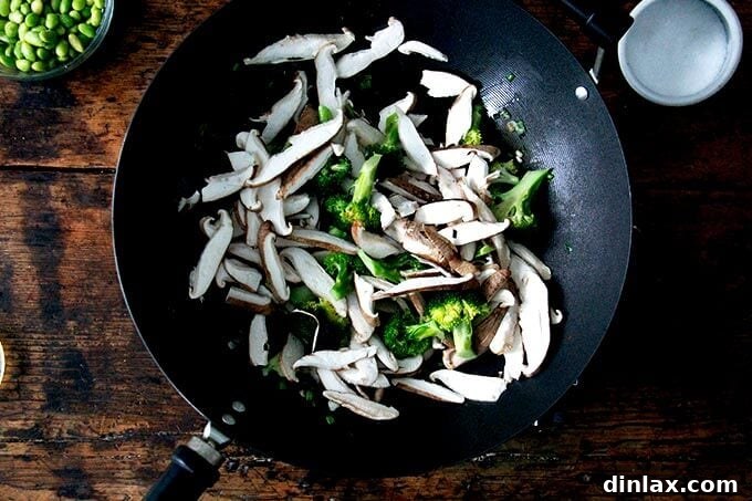 Sliced shiitake mushrooms are added to the stir-frying broccoli in the wok, merging their earthy flavors with the vibrant green.