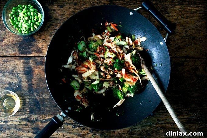 The vibrant red kimchi is introduced to the wok, mixing with the broccoli and shiitake mushrooms, ready to infuse the dish with its signature tang.