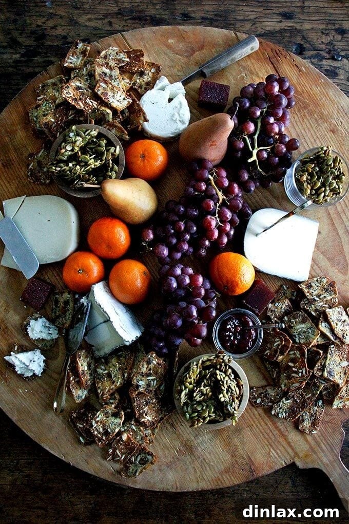 Three Seed Crisps 2 A beautifully arranged large cheese board featuring an assortment of cheeses, fresh grapes, vibrant oranges, a sliced pear, and delicious candied pepitas, alongside homemade crackers.