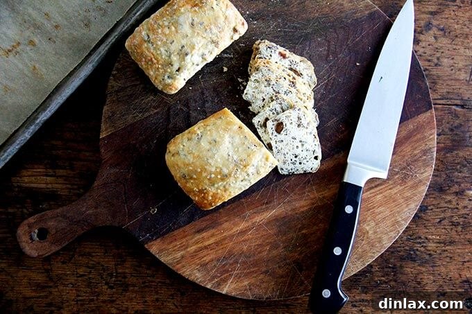 Three Seed Crisps 13 A collection of three-seed cracker loaves, expertly sliced into thin, uniform pieces, displayed on a cutting board.