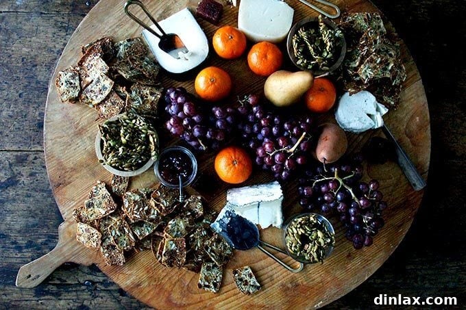 Three Seed Crisps 20 An opulent cheese board laden with a generous spread of homemade three-seed crackers, fresh green grapes, juicy orange segments, tender pear slices, and crispy candied pepitas.