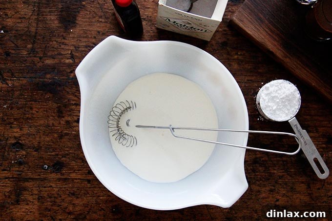 A large bowl filled with heavy cream and a wire whip.