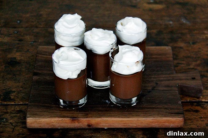 A board filled with small glasses filled with chocolate pot de creme and topped with homemade whipped cream.