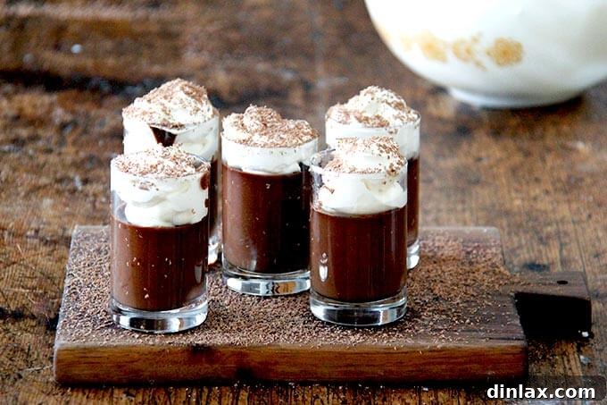 A board filled with small glasses filled with chocolate pot de creme and topped with homemade whipped cream and shaved chocolate over top.