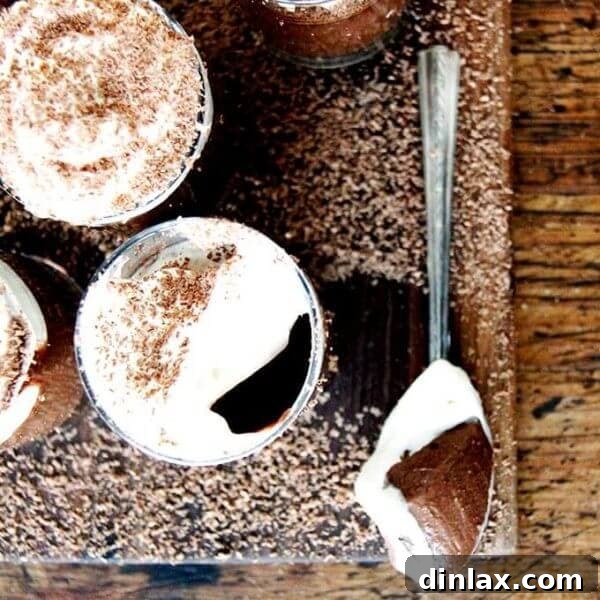A board filled with small glasses filled with chocolate pot de creme and topped with homemade whipped cream.