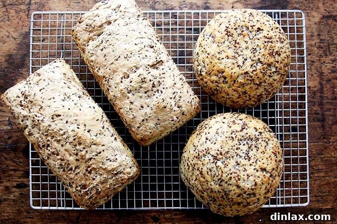 Golden Quinoa Flax Toast 17 Various loaves of just-baked quinoa-flax bread, including Pullman-style and round loaves, cooling on a rack.