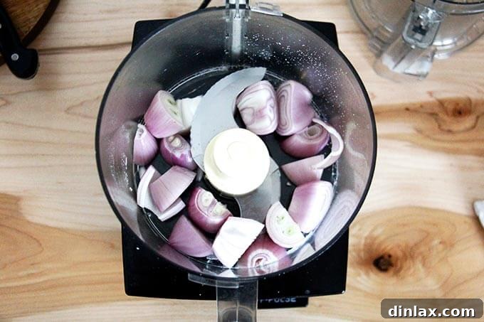Peeled and coarsely chopped shallots placed inside the food processor bowl, poised for quick mincing.