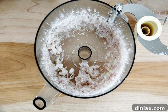 Finely minced shallots, processed to a perfect consistency, filling the bottom of a food processor bowl.