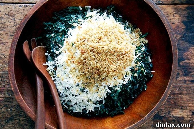 An overhead shot of an untossed kale salad in a large serving bowl, featuring a colorful mix of finely chopped kale, grated Parmesan, and golden breadcrumbs, with dressing yet to be added.