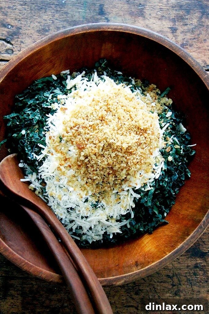 A close-up overhead shot of a vibrant, untossed kale salad in a large bowl, showcasing the fresh kale, generous grated Parmesan, and crunchy breadcrumbs before the dressing is incorporated.