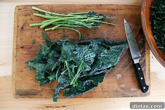 Hands carefully stripping the vibrant green leaves of Tuscan kale from their tough central stems on a wooden board.