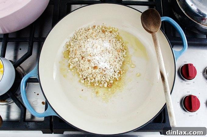 Golden-brown breadcrumbs being toasted in a skillet with shimmering olive oil, creating a fragrant, crunchy addition to the salad.
