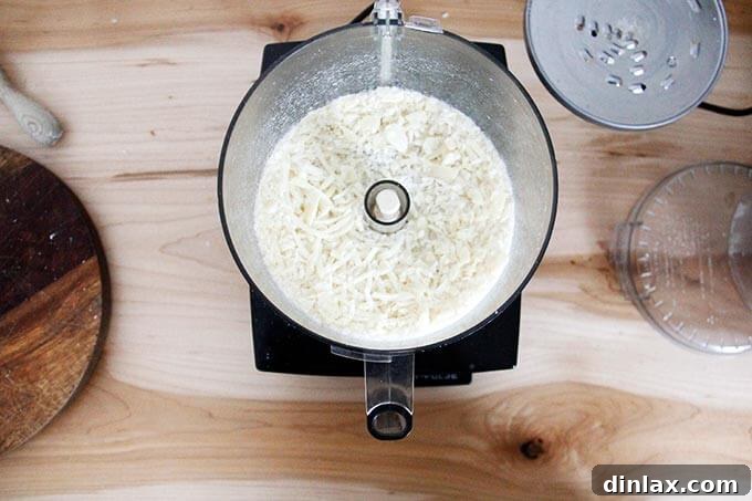 Large chunks of Parmigiano Reggiano cheese being grated within the food processor bowl, yielding fine, fresh cheese.