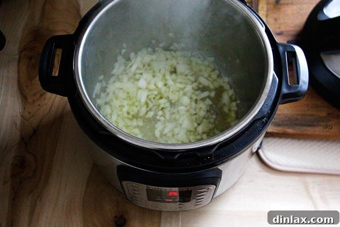 Instant Pot Harissa Rice with Sweet Dates and Zesty Orange 16 An overhead view of an Instant Pot insert, with chopped onions gently sautéing in olive oil, emitting fragrant steam.