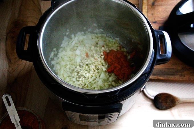 Instant Pot Harissa Rice with Sweet Dates and Zesty Orange 17 Inside an Instant Pot, a mixture of sautéed onions, minced garlic, and vibrant red harissa paste.
