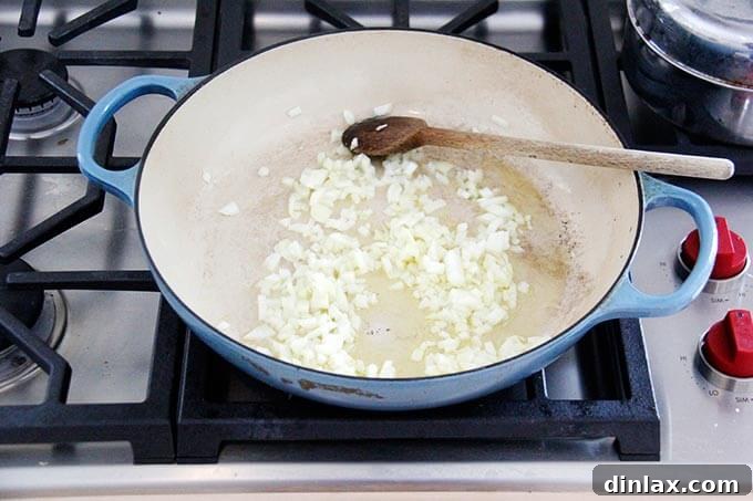 Instant Pot Harissa Rice with Sweet Dates and Zesty Orange 6 A large skillet on a stovetop, containing finely chopped onions gently sautéing in olive oil, turning translucent and fragrant.