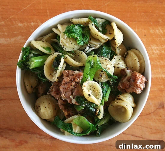 A comforting bowl of orecchiette pasta with hot Italian sausage, a vibrant mix of wilted greens, and a generous sprinkle of grated Parmigiano Reggiano cheese, ready to be enjoyed.