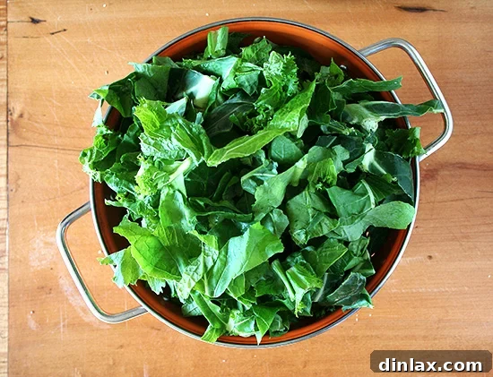 Freshly washed mixed greens draining in a colander, ready to be cooked.