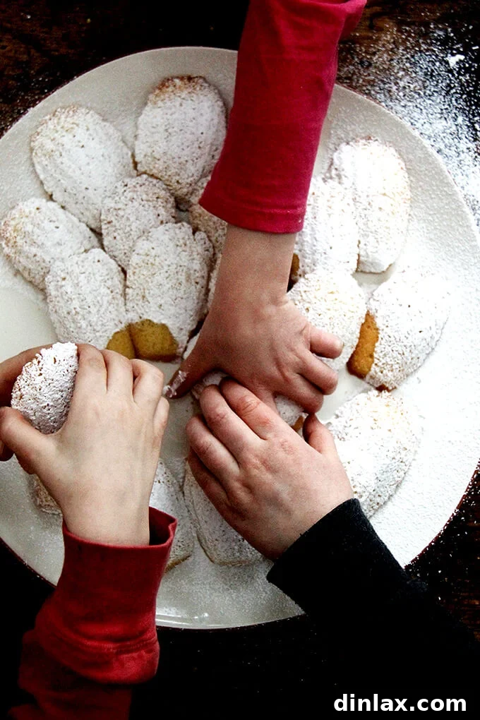 An overhead shot of multiple hands eagerly reaching into grab madeleines from a platter, illustrating their irresistible appeal.