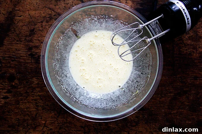 An overhead shot of a bowl of eggs beaten with sugar aside a hand-held mixer, showing the pale, fluffy mixture.