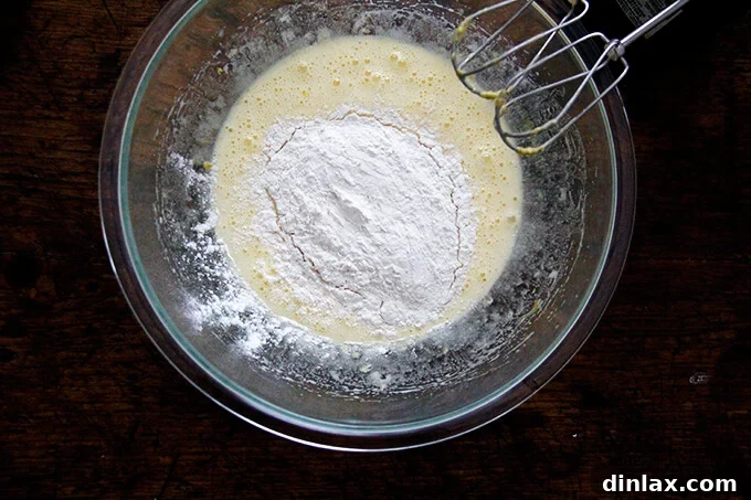 An overhead shot of a bowl of eggs beaten with sugar, lemon zest and flour, before mixing.