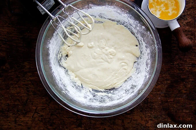 An overhead shot of a bowl of madeleine cookie batter aside a small sauce pan holding melted butter, ready to be incorporated.