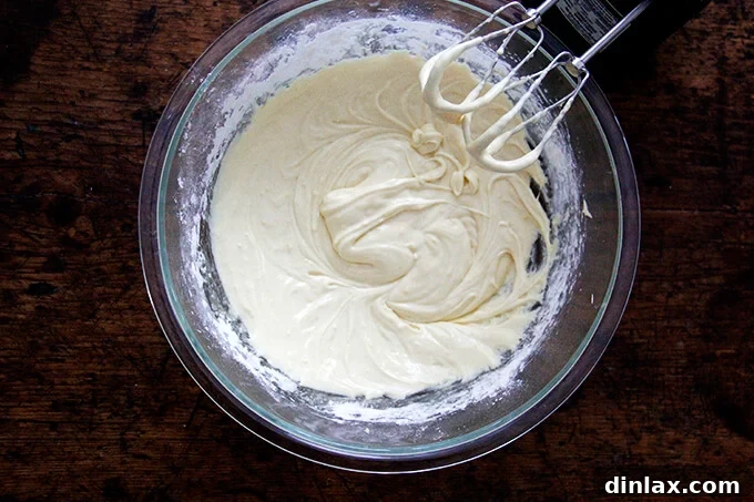 An overhead shot of a finished madeleine batter in a large bowl, now smooth and uniform, aside a hand-held mixer.