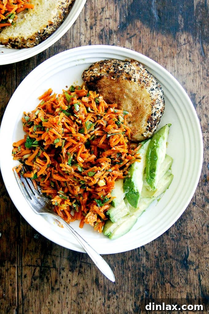 A beautifully arranged serving of Moroccan carrot salad in a bowl, accompanied by slices of creamy avocado and rustic bread.