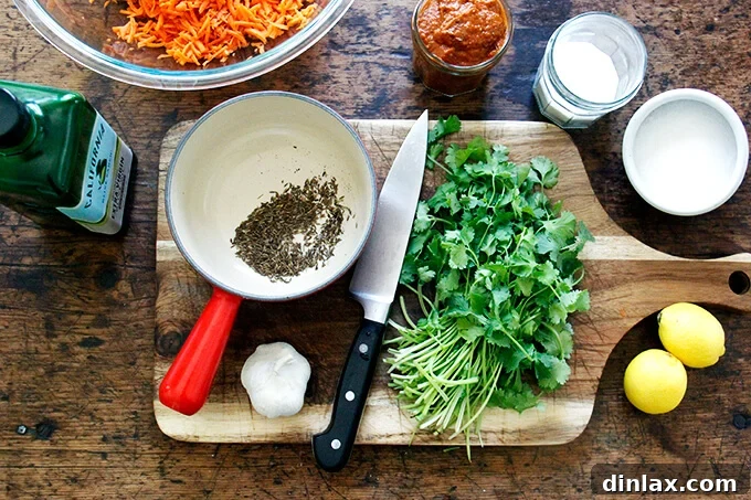 A selection of fresh ingredients including garlic cloves, cilantro, a lemon, and whole cumin seeds laid out on a wooden board.