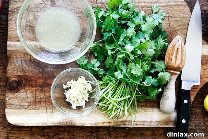 Minced garlic, fresh lemon halves, and finely chopped cilantro on a wooden board, prepared for the dressing.