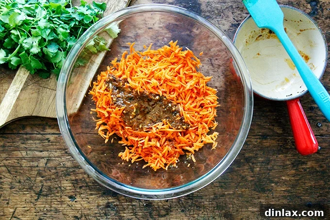 A large bowl of shredded carrots being tossed with the warm, red harissa dressing.