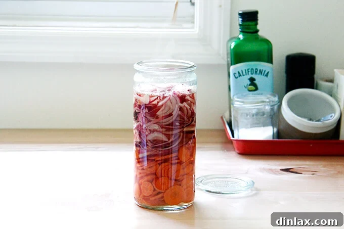 A jar filled with onions, carrots, and pickling liquid. 