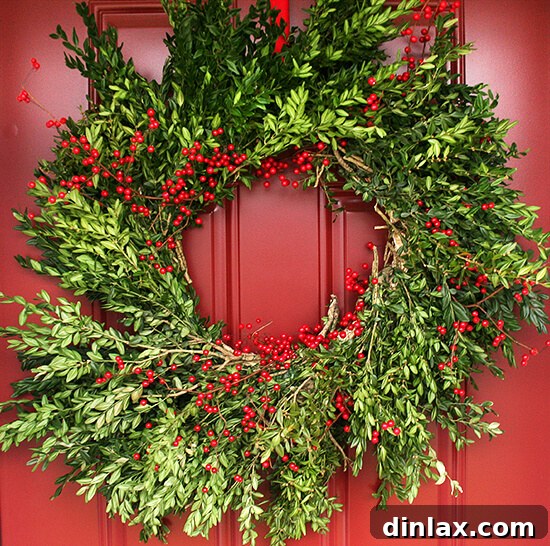 A handmade, rustic holiday wreath made from fresh green foliage and red holly berries, resting on a wooden surface.