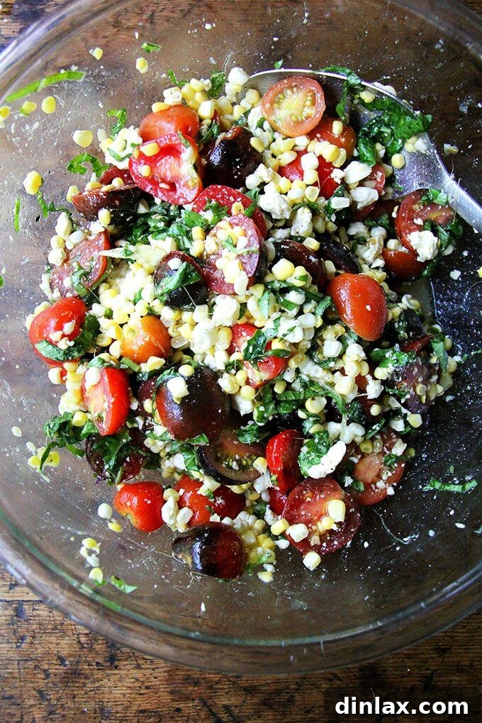 Vibrant raw corn and tomato salad with feta and fresh herbs, showcasing summer produce.