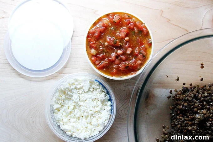 Containers of fresh bruschetta sauce and crumbled feta, alongside a bowl of cooked lentils, all opened and ready to be combined.