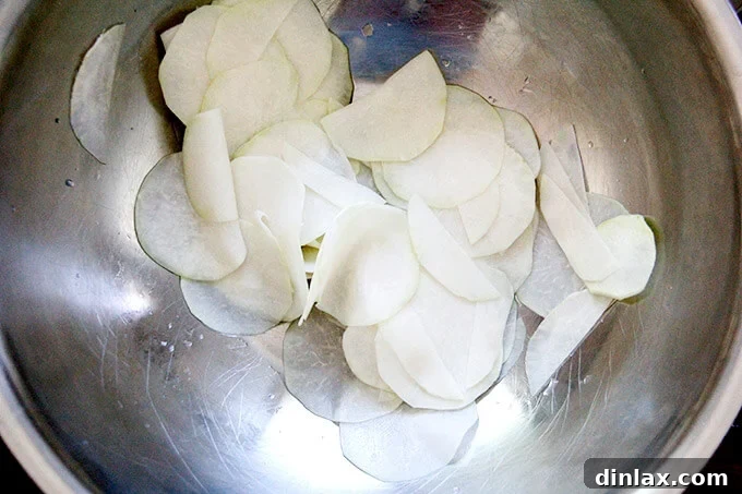 Thinly shaved kohlrabi in a large bowl, seasoned with salt and vinegar, beginning to soften. The first step in creating a tender salad.