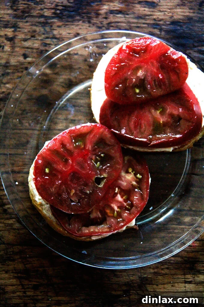 A plate featuring a halved bagel, generously topped with cream cheese, sliced tomatoes, and a sprinkle of salt, ready to be enjoyed.