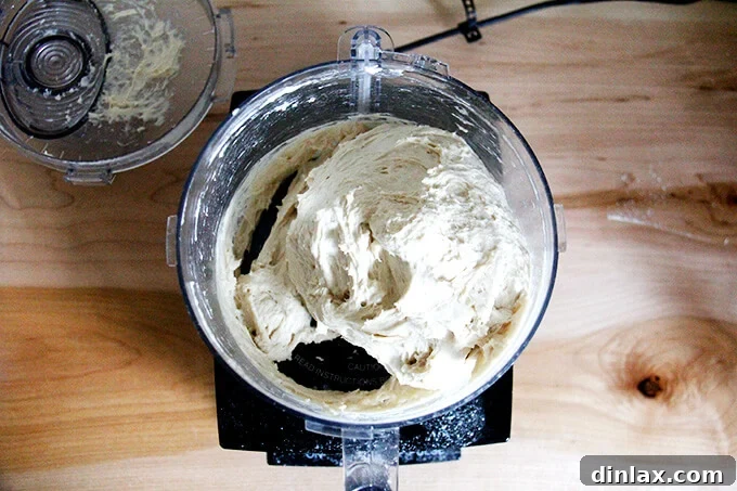 Dense bagel dough actively kneading in a food processor, highlighting the rapid dough development.